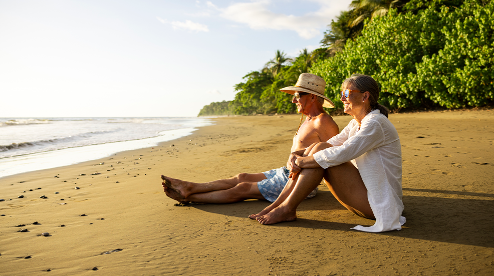 A senior couple sitting on a beach and watching sunset